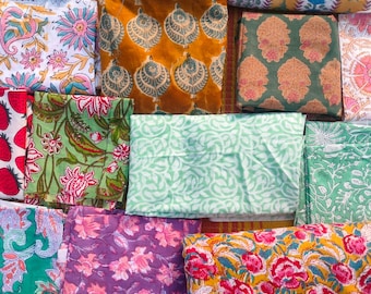 Könnte beinhalten: Eine Sammlung gefalteter Stoffquadrate mit verschiedenen floralen und geometrischen Mustern. Die Farben umfassen Türkis, Rosa, Gelb, Grün und Lila. Die Stoffe scheinen aus Baumwolle oder einem ähnlichen Material zu bestehen, das sich für Quilt- oder Bastelprojekte eignet.