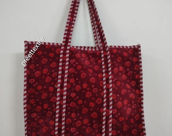 May include: A burgundy tote bag with a floral pattern and striped accents. The bag has a rectangular shape with a matching handle. The floral pattern is composed of small red flowers.