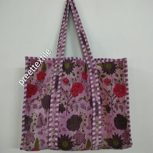 Puede incluir: Un bolso tote acolchado con un estampado floral en tonos rosa, morado y verde. El bolso presenta un patr&oacute;n repetido de rosas y otras flores. Las asas y los bordes est&aacute;n ribeteados con una tela a rayas. El texto "preette textile" est&aacute; impreso en el lateral del bolso.
