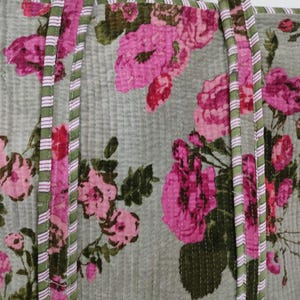 Puede incluir: Bolso tote acolchado con estampado floral. El bolso presenta grandes rosas rosas sobre un fondo verde claro. Las asas y los bordes est&aacute;n ribeteados con tela a rayas verdes y rosas. El bolso tiene un dise&ntilde;o acolchado vertical.