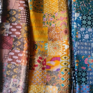 May include: Close-up of colorful patchwork fabric with floral and geometric patterns. The fabric features a mix of warm and cool tones, including yellow, orange, brown, and blue. The design is reminiscent of vintage textiles.