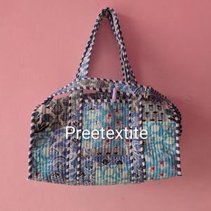 Peut inclure: Un sac de voyage matelassé avec un motif patchwork dans des tons de bleu et blanc, agrémenté de motifs floraux et géométriques. Le sac possède deux anses et une bandoulière avec une bordure rayée. Le texte Preetextite est imprimé devant.