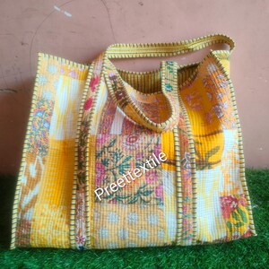 Op de afbeelding: Een grote, gewatteerde draagtas met een patchwork-ontwerp. De tas heeft een mix van gele, witte en bloemmotiefstoffen. De tekst "Preettextile" is zichtbaar op de voorkant. De tas heeft een bijpassende gele handgreep en afwerking.
