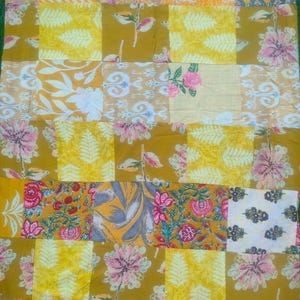 May include: A patchwork quilt featuring a variety of floral and geometric patterns in shades of yellow, orange, pink, and green. The quilt is made of individual fabric squares sewn together, creating a vibrant and textured design. The quilt is a decorative home textile.
