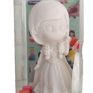 Può includere: Un salvadanaio bianco non dipinto a forma di ragazza con capelli intrecciati e un abito lungo, confezionato in una scatola di plastica trasparente con piccoli vasetti di vernice. La base riporta il testo "Cute Girl Piggy Bank" in lettere colorate.