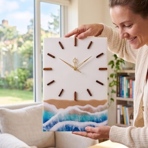 May include: Rectangular wall clock with a white face, gold hands, and brown wooden markers. The bottom of the clock features a beach scene with blue waves and tan sand. The clock measures approximately 12 inches by 16 inches.