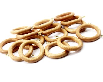 Könnte beinhalten: Eine Ansammlung hellbrauner Gardinenringe aus Holz, jeweils mit einer kleinen messingfarbenen Öse. Die Ringe sind kreisförmig und haben eine glatte, natürliche Oberfläche. Sie liegen auf weißem Hintergrund, für Heimdekoration.