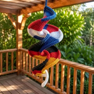 May include: A spiral-shaped hanging decoration crafted from crocheted yarn. The design features alternating segments of red, white, blue, black, and yellow, creating a continuous twisted pattern that hangs vertically from a single blue yarn loop.