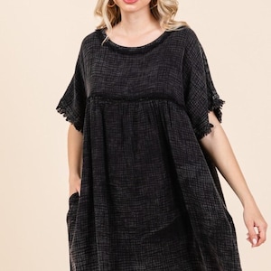 May include: Black short-sleeve dress with a textured pattern. The dress features a round neckline, pockets, and fringe detailing on the sleeves. The dress is knee-length and has a loose, comfortable fit.