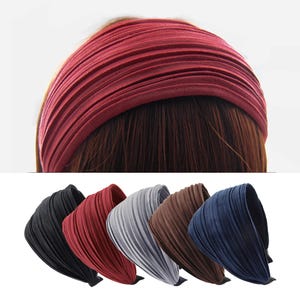 Può includere: Una collezione di fasce per capelli plissettate in vari colori, tra cui nero, rosso, grigio, marrone e blu navy. Le fasce sono realizzate in un tessuto morbido e strutturato e sono progettate per essere indossate sulla fronte.
