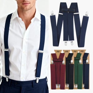 Puede incluir: Tirantes azul marino con clips plateados, mostrados en una persona con camisa blanca y pantalón azul marino. Tirantes adicionales en burdeos, negro, verde y azul marino en embalaje de cartón.