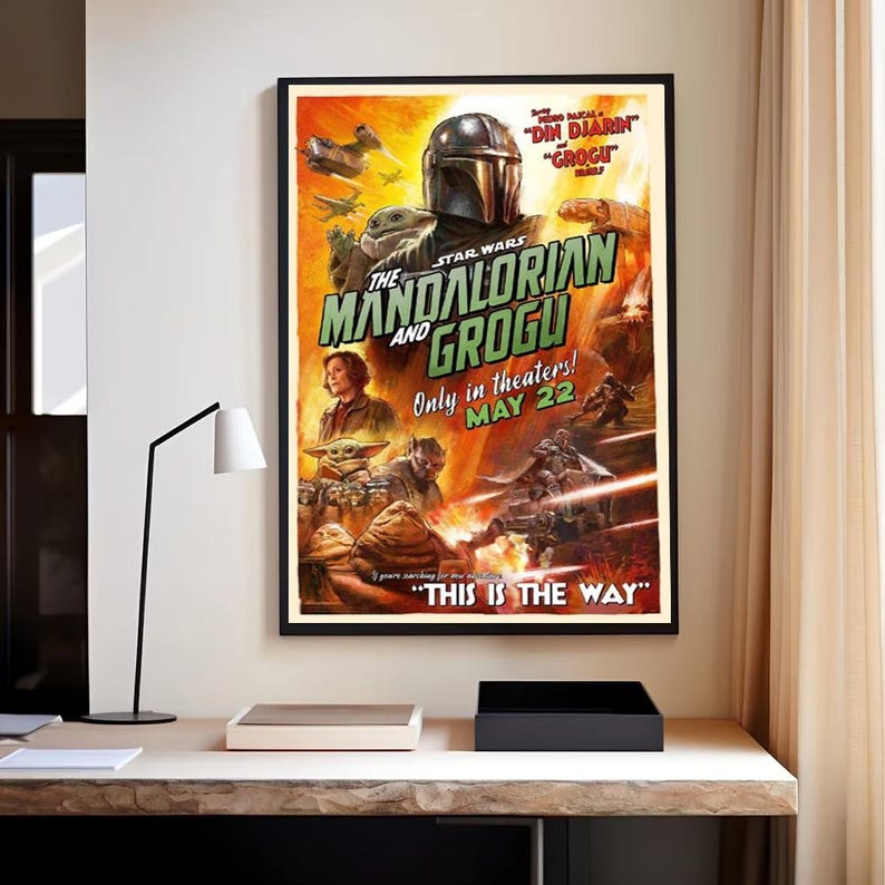 May include: Framed movie poster for "The Mandalorian and Grogu" in a black frame. The poster shows a helmeted character, Grogu, and other characters against a fiery orange and yellow backdrop. Text includes "Only in theaters! MAY 22" and "THIS IS THE WAY."