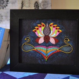 May include: A framed painting of a colorful lotus flower with peacocks on either side. The lotus has pink petals and a dark purple center. The peacocks are black with gold accents. The background is a dark blue.