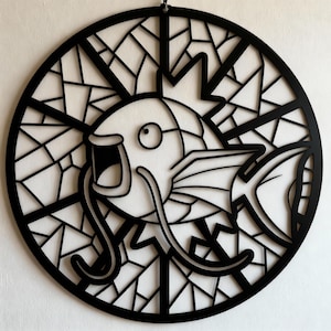 May include: Black, circular wall art featuring a stylized fish design. The fish is set against a geometric background, with a crown-like detail on its head. The art piece is made of cut-out shapes, creating a layered effect.