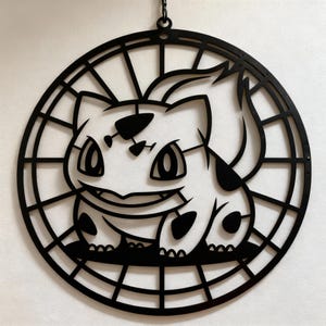 May include: Black metal wall art featuring a cartoon character within a circular frame. The character has large eyes, a smiling mouth, and spots. The art is designed with a cut-out style, creating a silhouette.