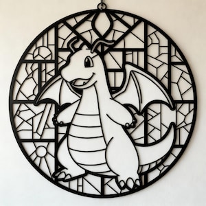 May include: Black and white dragon-themed wall art. The design features a smiling dragon in the center, surrounded by a stained-glass style frame. The dragon has wings and a long tail. The artwork is circular and hangs from a small chain.