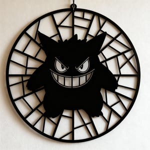 May include: Black silhouette of a cartoon character with a wide grin and pointed ears, set within a circular, web-like frame. The character's eyes are white with a menacing expression. The artwork is designed to be hung.