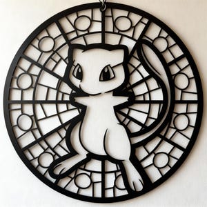 May include: Black circular wall art featuring a white Mew character design. The design is set within a stained-glass style frame with geometric shapes. The artwork is likely made of cut metal or wood, and is suitable for home decor.