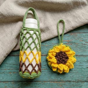 May include: A handmade crochet water bottle holder and a matching sunflower coaster. The bottle holder is green, yellow, and brown, with a handle. The coaster is yellow and brown, resembling a sunflower. Both items are on a teal wooden surface.