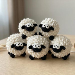 May include: Five handmade crochet sheep toys. Each sheep has a fluffy white body, black face, and black legs. The sheep are arranged on a light-colored wooden surface, suggesting a craft or nursery theme.