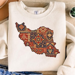 May include: Cream-colored sweatshirt featuring a detailed map of Iran, filled with intricate patterns in red, blue, and gold. The design resembles a patchwork of traditional rug motifs, offering a cultural and artistic statement.