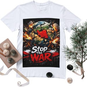 May include: White t-shirt featuring a graphic of a fractured globe with a red center, surrounded by explosions. The words "Stop the War" are prominently displayed in white and red. The design is centered on the shirt.