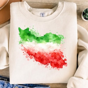 May include: Cream-colored sweatshirt featuring a watercolor design of the Iran map in green, white, and red. The graphic has a splattered paint effect. The sweatshirt is made of a soft material.