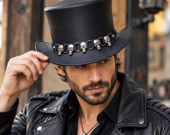 May include: A black leather top hat featuring a decorative band adorned with a series of metallic silver-toned skull ornaments. The hat has a structured cylindrical crown and a curved brim, providing a distinct appearance.