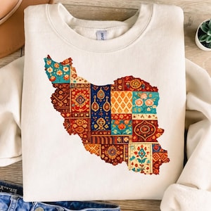 Op de afbeelding: Crèmekleurige sweatshirt met een kleurrijk patchwork-ontwerp in de vorm van Iran. Het patchwork bevat bloemen- en geometrische patronen in tinten rood, blauw, oranje en groen.