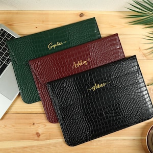 May include: Three personalized laptop sleeves in green, burgundy, and black, with a faux crocodile skin texture. Each sleeve has a name in gold script: Sophia, Ashley, and Anna. The sleeves are on a wooden surface, near a laptop and a coffee cup.