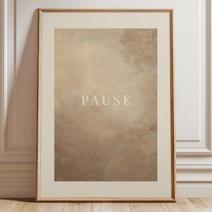 Puede incluir: Impresión artística enmarcada con un diseño abstracto texturizado en tonos beige y marrón. La palabra "PAUSE" está centrada en blanco, con una fuente sans-serif. La obra de arte está encerrada en un marco dorado, añadiendo un toque de elegancia.