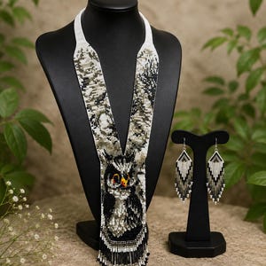 Könnte beinhalten: Ein Set aus einer Perlenkette und passenden Ohrringen mit einem detaillierten Eulenmotiv. Der Schmuck besteht aus weißen, schwarzen, grauen und orangefarbenen Glasperlen. Die lange Kette hat einen Fransenabschluss und die Ohrringe sind dreieckig.