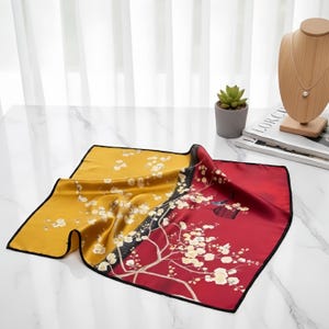 Peut inclure: Un foulard carr&eacute; en soie avec un motif floral. Le foulard pr&eacute;sente un design en blocs de couleurs avec des sections jaunes et rouges, s&eacute;par&eacute;es par une bordure noire. Des motifs floraux blancs sont imprim&eacute;s sur le foulard.