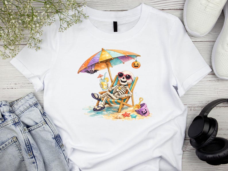 May include: A white t-shirt featuring a graphic of a skeleton wearing pink sunglasses, relaxing in a beach chair under a colorful striped umbrella. The skeleton holds a yellow drink, with a small bat, a jack-o'-lantern, and a purple bucket nearby.