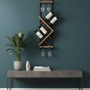 May include: A contemporary wine rack featuring a black metal frame and natural wood detailing, designed to hold four wine bottles and two wine glasses. The rack is mounted on a teal wall, with a potted plant and a grey console table in the foreground.