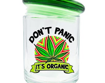 May include: A clear glass jar with a green lid. The jar features the text "DON'T PANIC" above a green cannabis leaf design with red, yellow, and green accents. Below the leaf is the text "IT'S ORGANIC".