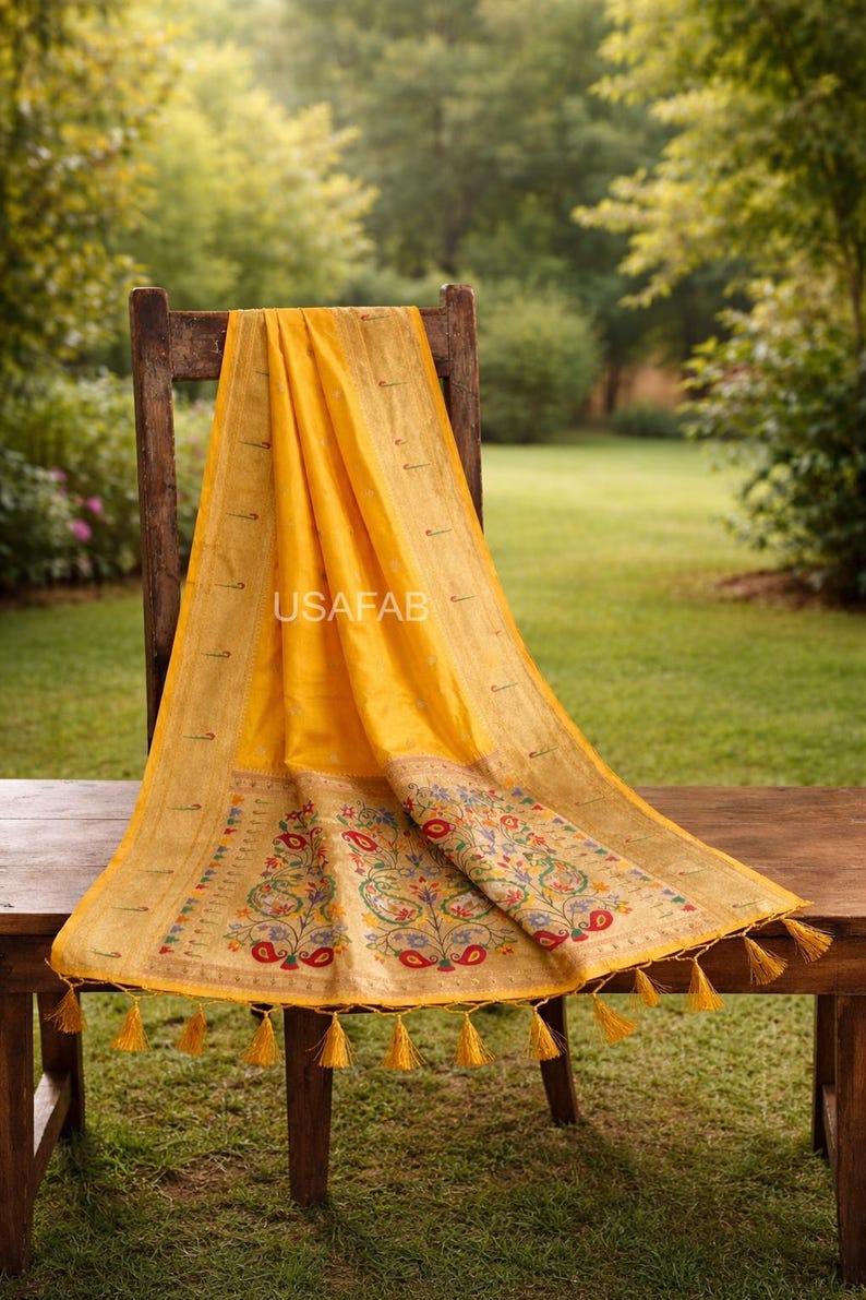 Puede incluir: Un textil amarillo vibrante con intrincados dise&ntilde;os florales y de cachemira, drapeado sobre una silla de madera. El textil presenta un borde detallado y borlas decorativas. El texto "USAFAB" es visible.