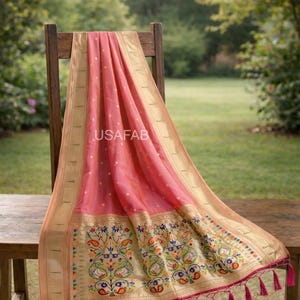 Puede incluir: Un textil rosa con borde dorado y bordado floral detallado. La tela est&aacute; drapeada sobre una silla de madera, mostrando un dise&ntilde;o con acentos coloridos y borlas rosas. El texto "USAFAB" es visible.