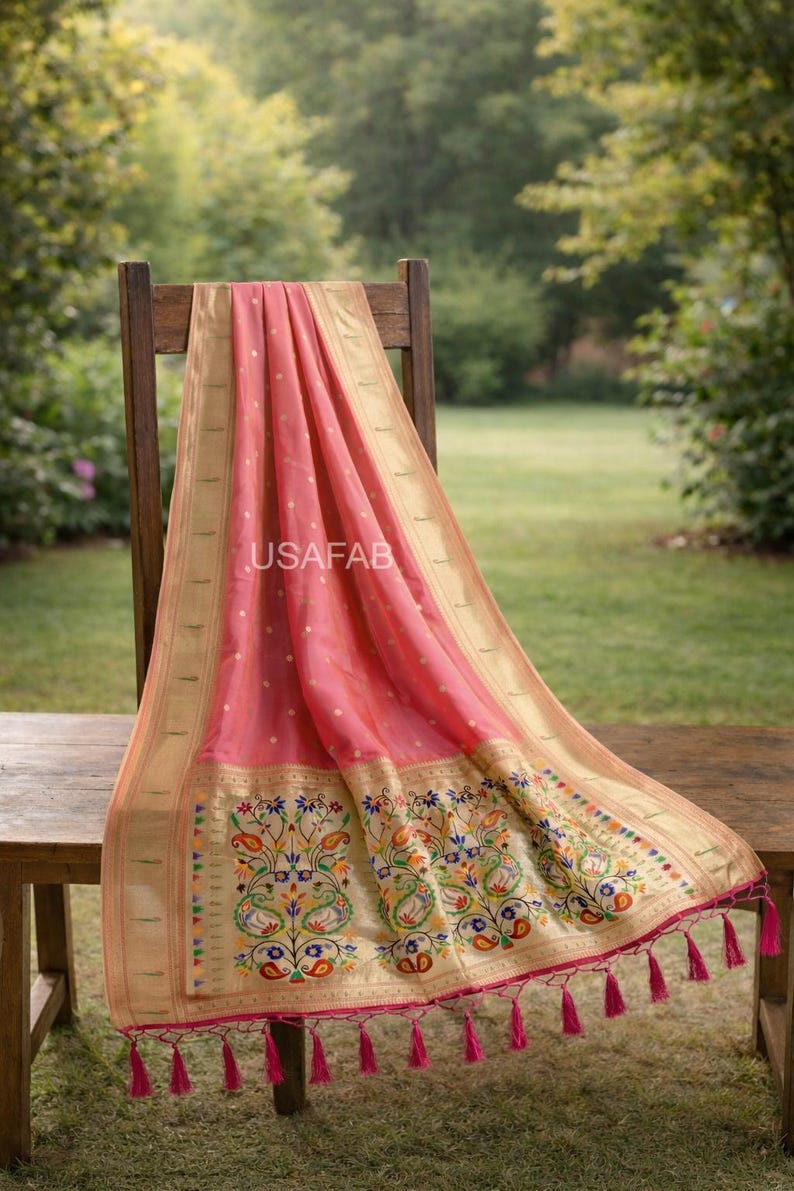 Puede incluir: Un textil rosa con borde dorado y bordado floral detallado. La tela est&aacute; drapeada sobre una silla de madera, mostrando un dise&ntilde;o con acentos coloridos y borlas rosas. El texto "USAFAB" es visible.