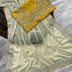 May include: A light green saree with a mustard yellow blouse. Both are decorated with pink, green, and gold floral embroidery. The saree has the text "USAFAB".
