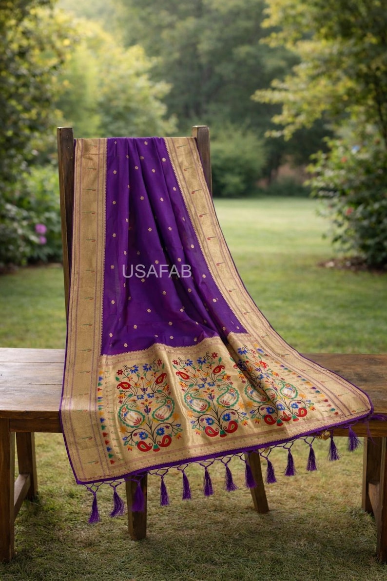 Puede incluir: Un textil morado vibrante con bordes dorados y intrincados dise&ntilde;os florales. La tela est&aacute; drapeada sobre una silla y una mesa de madera, mostrando un dise&ntilde;o detallado con acentos coloridos y borlas. El texto "USAFAB" es visible.