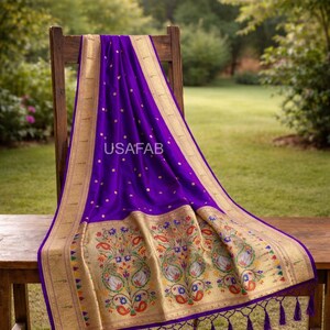 Puede incluir: Un textil morado vibrante con bordes dorados y bordados florales intrincados. La tela est&aacute; drapeada sobre un banco y una silla de madera, mostrando el dise&ntilde;o detallado y la textura. El texto "USAFAB" es visible en la tela.