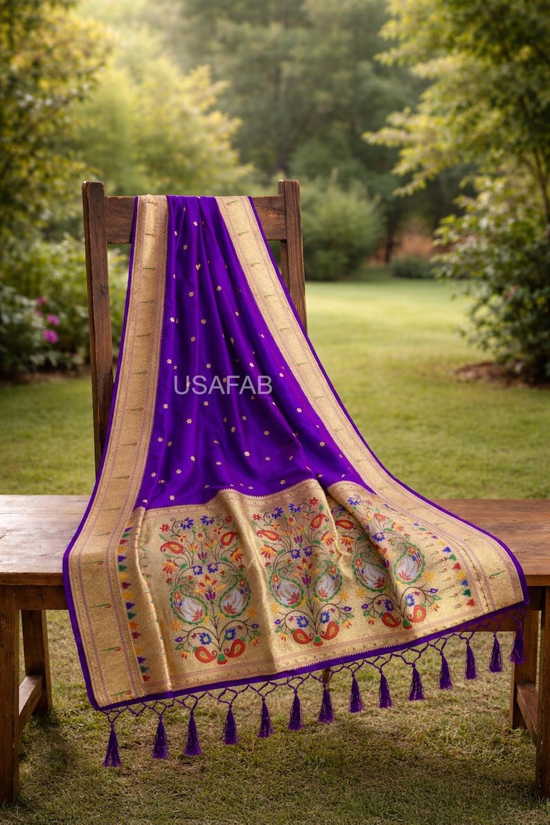 Puede incluir: Un textil morado vibrante con bordes dorados y bordados florales intrincados. La tela est&aacute; drapeada sobre un banco y una silla de madera, mostrando el dise&ntilde;o detallado y la textura. El texto "USAFAB" es visible en la tela.