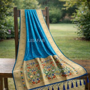 Puede incluir: Un textil azul con un borde dorado y un intrincado bordado floral, drapeado sobre una silla de madera. El textil presenta un patr&oacute;n repetitivo de puntos blancos y un borde decorativo con borlas. El texto ".USAFAB" es visible.