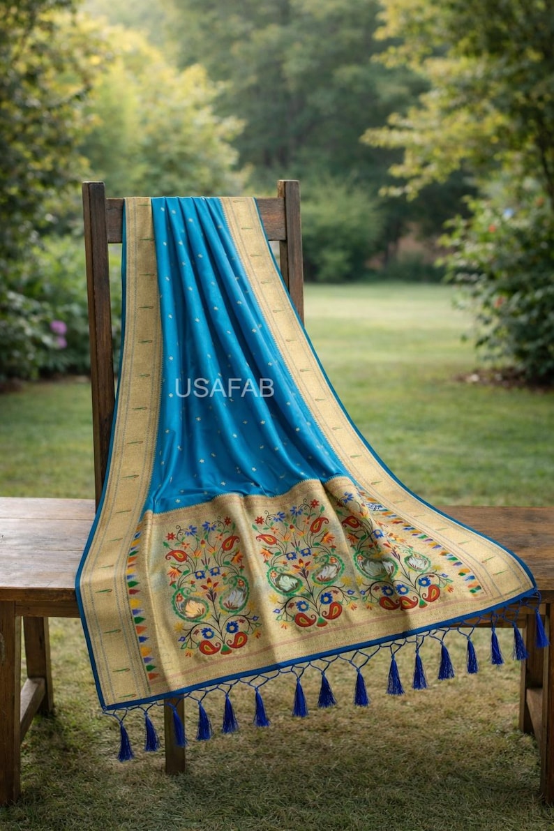 Puede incluir: Un textil azul con un borde dorado y un intrincado bordado floral, drapeado sobre una silla de madera. El textil presenta un patr&oacute;n repetitivo de puntos blancos y un borde decorativo con borlas. El texto ".USAFAB" es visible.