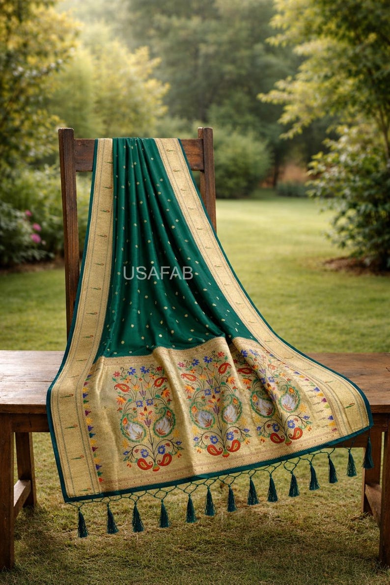 Puede incluir: Textil verde esmeralda con ribete dorado y bordados florales, drapeado sobre una silla de madera. El textil presenta un borde detallado con dise&ntilde;os florales y paisley coloridos. El texto "USAFAB" es visible.
