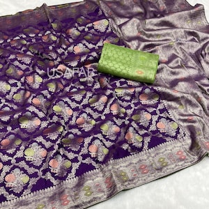 May include: A luxurious purple saree with intricate floral patterns in pink, green, and silver. The saree features a detailed border and a matching green fabric piece. The text "USAFAB" is visible on the saree.
