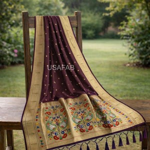 Puede incluir: Un textil burdeos oscuro con bordes dorados y bordados florales, drapeado sobre una silla de madera. El textil presenta un patr&oacute;n repetido de peque&ntilde;os puntos dorados y el texto "USAFAB". El borde inferior tiene borlas moradas.