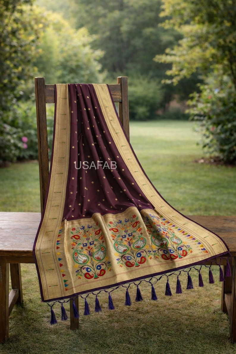 Puede incluir: Un textil burdeos oscuro con bordes dorados y bordados florales, drapeado sobre una silla de madera. El textil presenta un patr&oacute;n repetido de peque&ntilde;os puntos dorados y el texto "USAFAB". El borde inferior tiene borlas moradas.