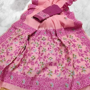 Może przedstawiać: Różowe sari z kwiatowym wzorem i pasującym fioletowym kawałkiem bluzki. Sari ma szczegółowy wzór obramowania i dekoracyjne frędzle wzdłuż krawędzi. Tkanina wydaje się miękka i lekka, odpowiednia do tradycyjnego noszenia.